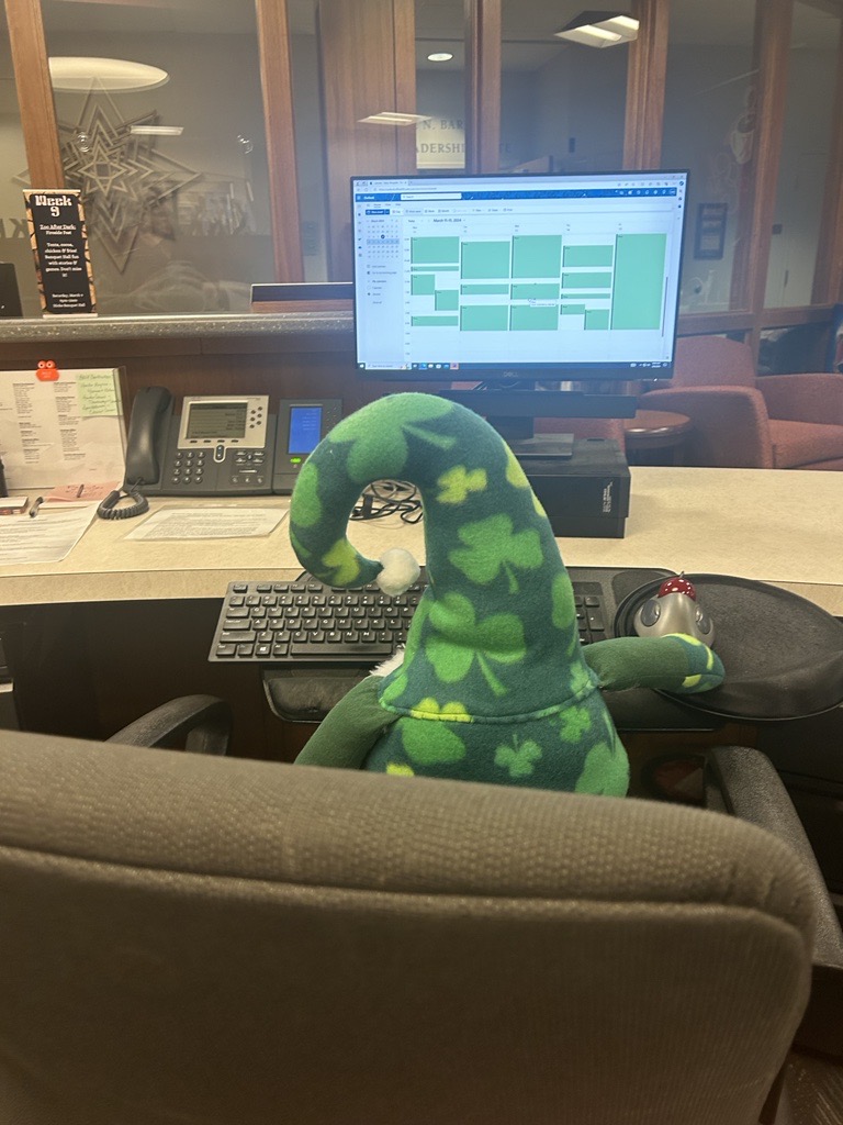 Image of Jerome the leprechaun (a green shamrock patterned hat) shown looking at a computer screen with a weekly calendar displayed. 
